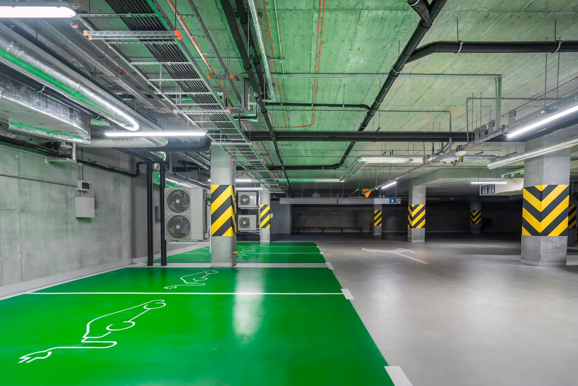 Parking subterráneo con plazas de aparcamiento con suelo de color verde y símbolo de coche eléctrico.